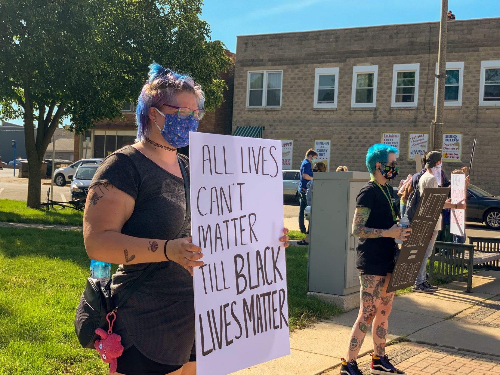 A protester holds a sign that says, "All lives can't matter 'til black lives matter' during a Kneel for Nine event on Wehmhoff Square in Burlington.