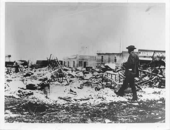 An African-American photographer  looking at the ruins of the Midway Hotel. The Goodner-Malone Co. is in the background. 