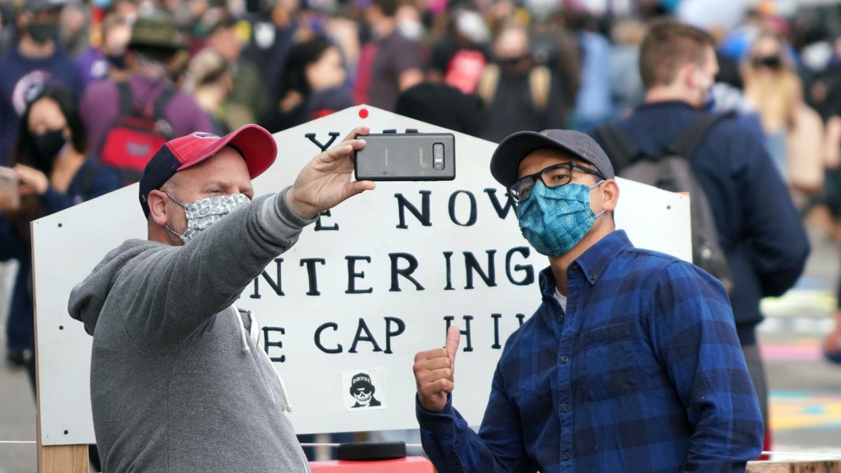 Two man take a picture in front of the Free Cap Hill sign in Seattle during a temporary occupation of what was also called the Capitol Hill Autonomous Zone.
