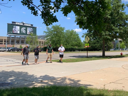 New Michigan State football defensive coordinator Scottie Hazelton, middle, prepares to cover his face with a bandana as he arrives with a group to go through COVID-19 testing Monday in East Lansing.