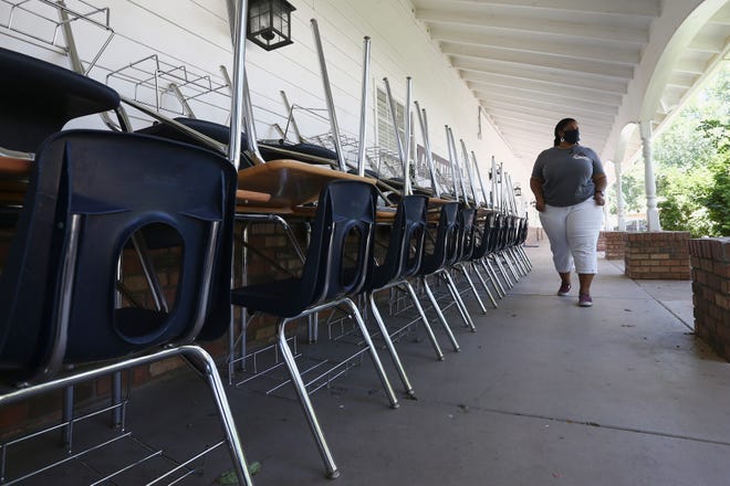 In this June 1, 2020 file photo, Kristina Washington, special education staff member at Desert Heights Preparatory Academy, walks past a series of desks and chairs at the school in Phoenix, returning to her classroom for only the second time since the coronavirus outbreak closed schools.