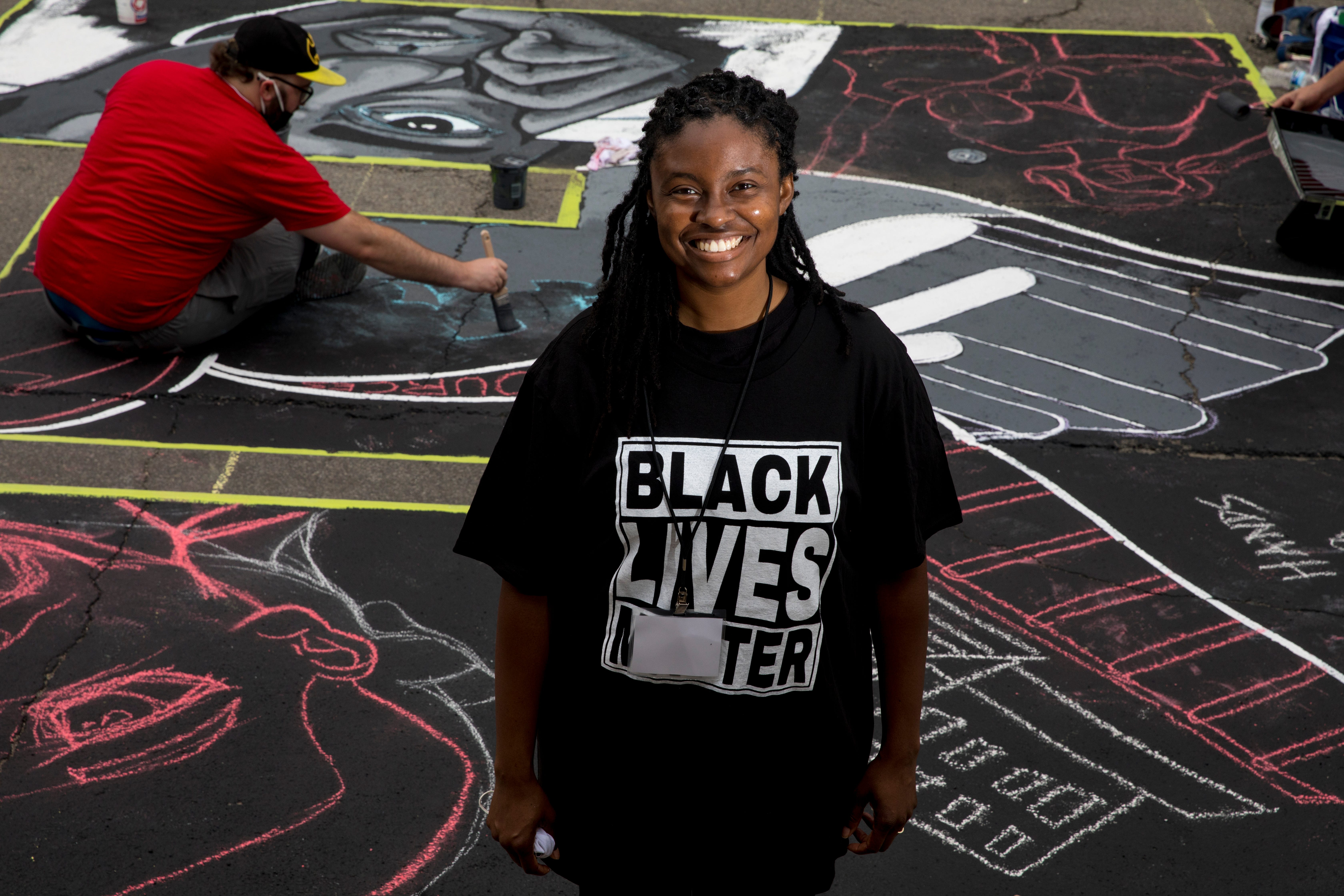 Latausha Cox stands next to the letter "E" that she is creating as part of a bigger mural that reads "Black Lives Matter!" Thursday, June 18, 2020, on Plum Street in front of City Hall in Cincinnati. Seventeen local Black artists were charged with designing and creating a letter to be part of the mural.