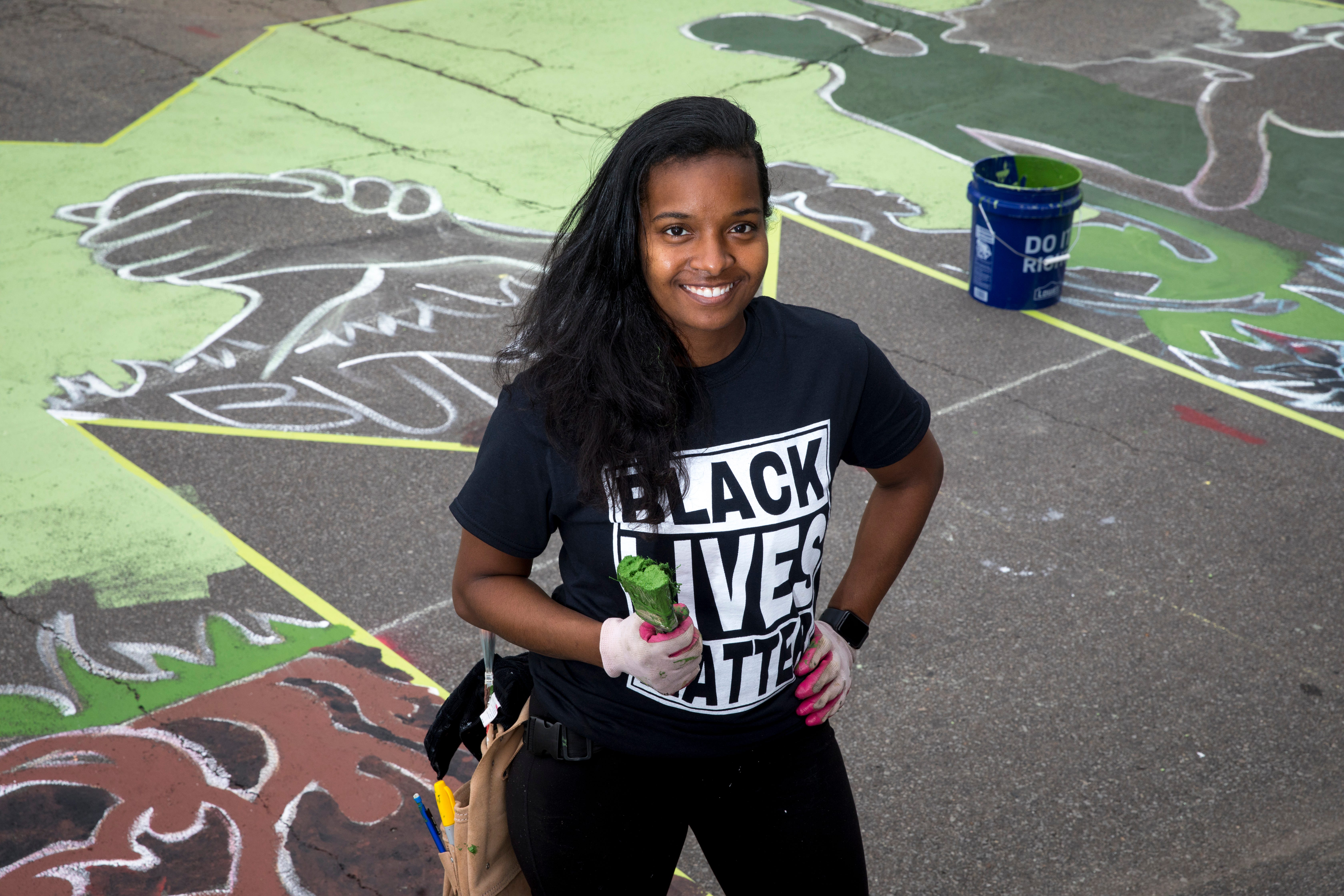 Adoria Maxberry stands next to the letter "M" that she is  creating as part of a bigger mural that reads "Black Lives Matter!" Thursday, June 18, 2020, on Plum Street in front of City Hall in Cincinnati. Seventeen local Black artists were charged with designing and creating a letter to be part of the mural. 