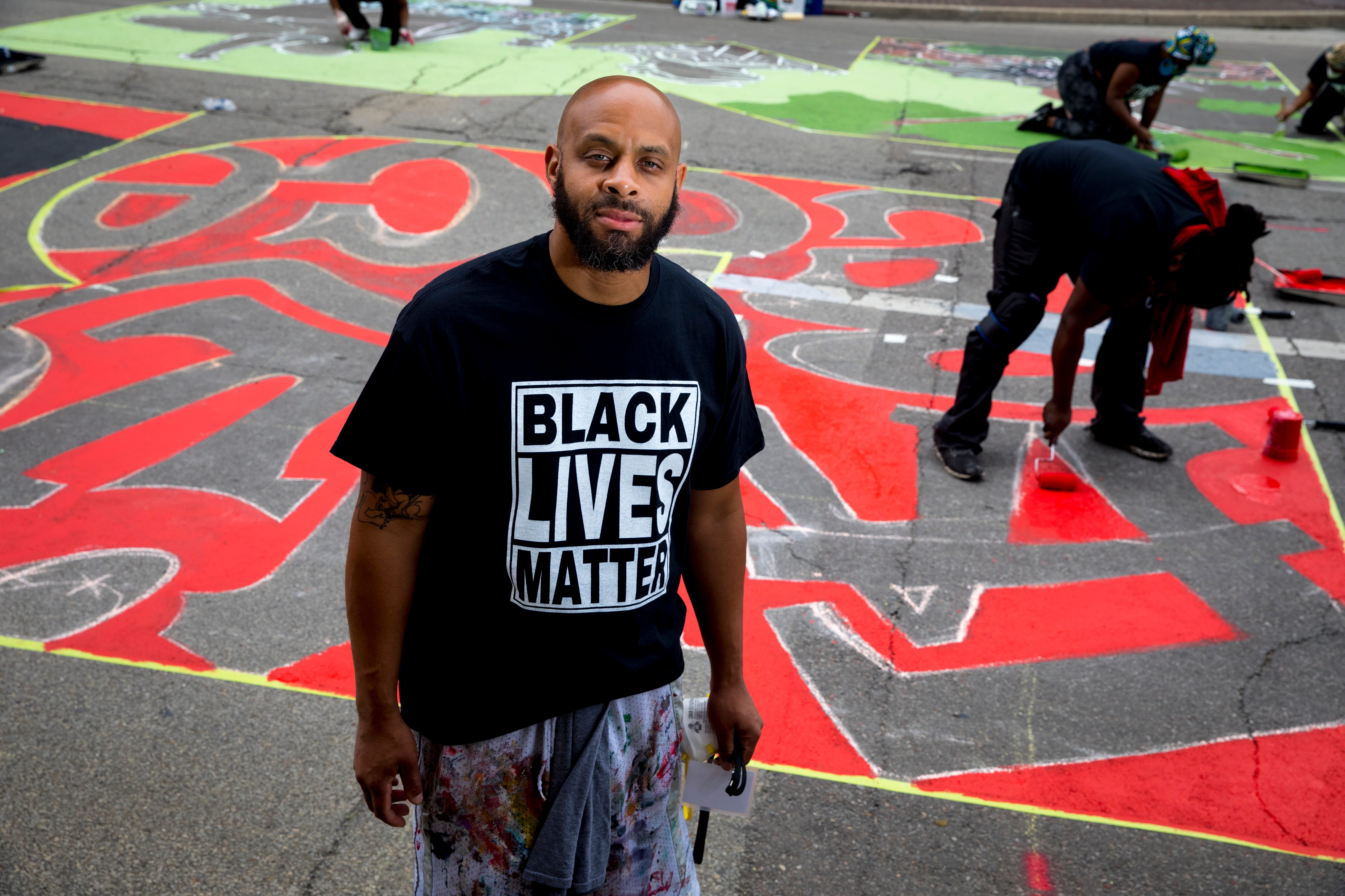 Brandon Hawkins stands next to the letter 'B' that he is creating as part of a bigger mural that reads "Black Lives Matter!" Thursday, June 18, 2020, on Plum Street in front of City Hall in Cincinnati. Seventeen local Black artists were charged with designing and creating a letter to be part of the mural.
