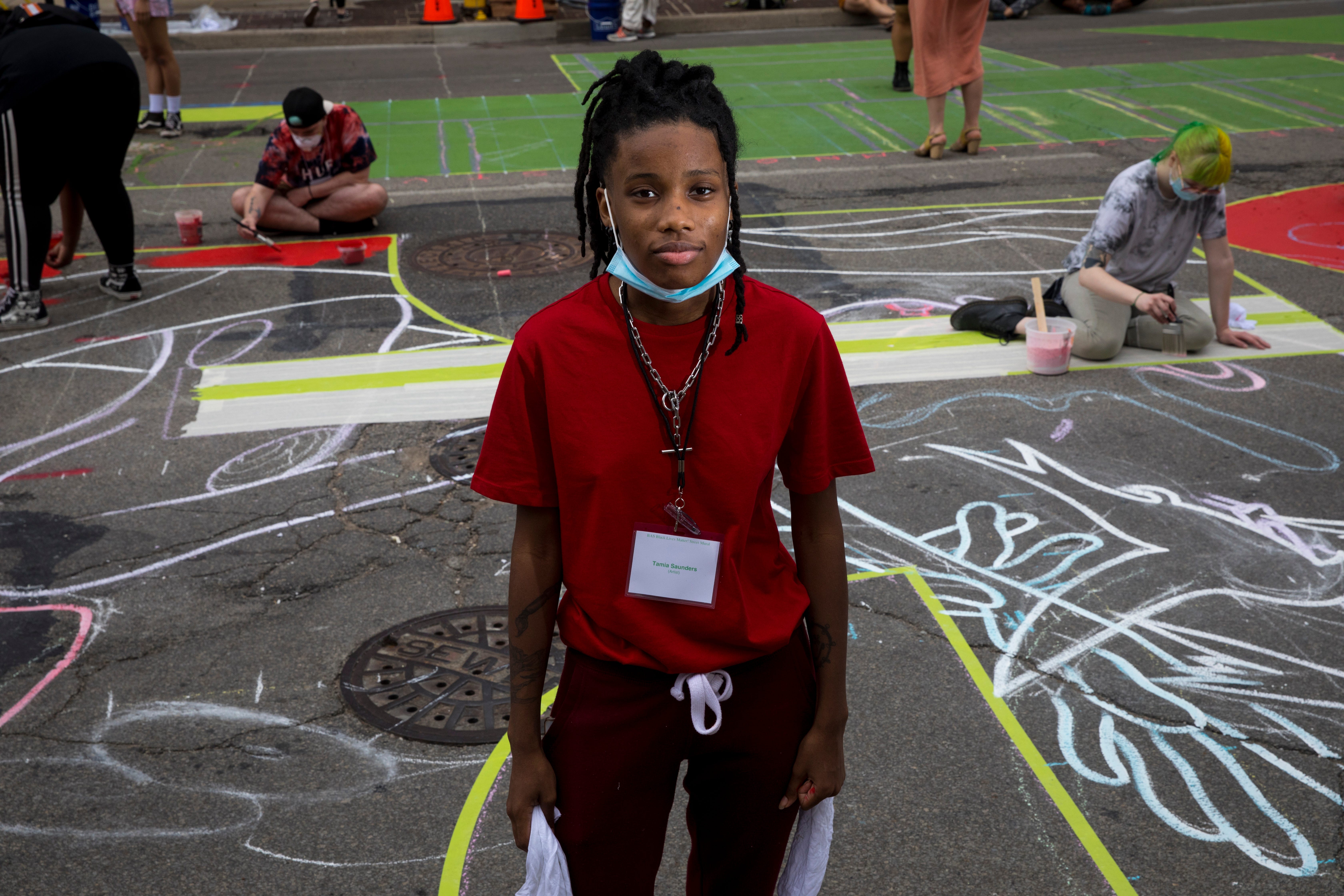 Tamia Saunders stands next to the letter "K" that she is creating as part of a bigger mural that reads "Black Lives Matter!" Thursday, June 18, 2020, on Plum Street in front of City Hall in Cincinnati. Seventeen local Black artists were charged with designing and creating a letter to be part of the mural. 