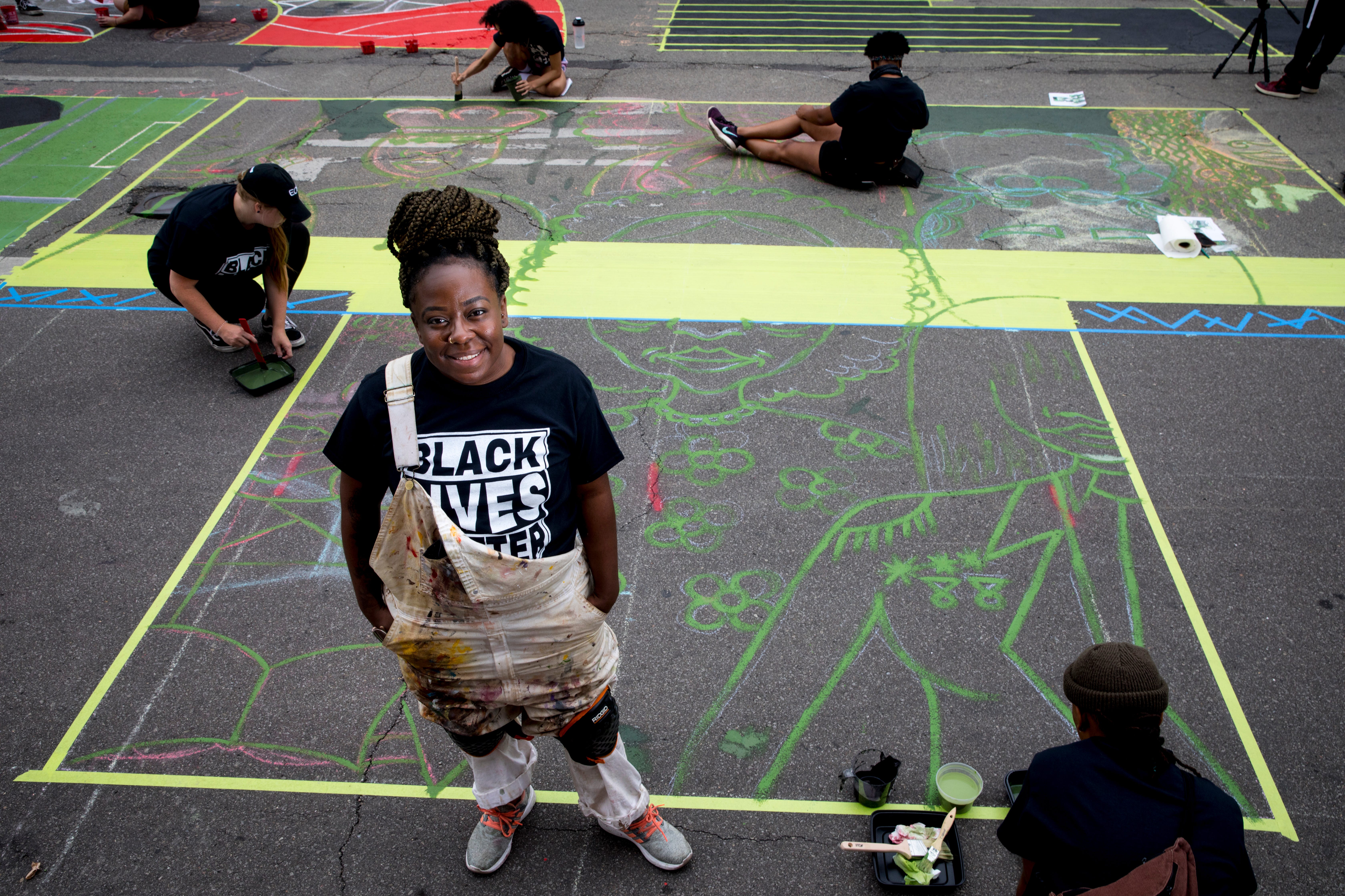 Asha White stands next to the letter "T" that she is creating as part of a bigger mural that reads "Black Lives Matter!" Thursday, June 18, 2020, on Plum Street in front of City Hall in Cincinnati. Seventeen local Black artists were charged with designing and creating a letter to be part of the mural. 