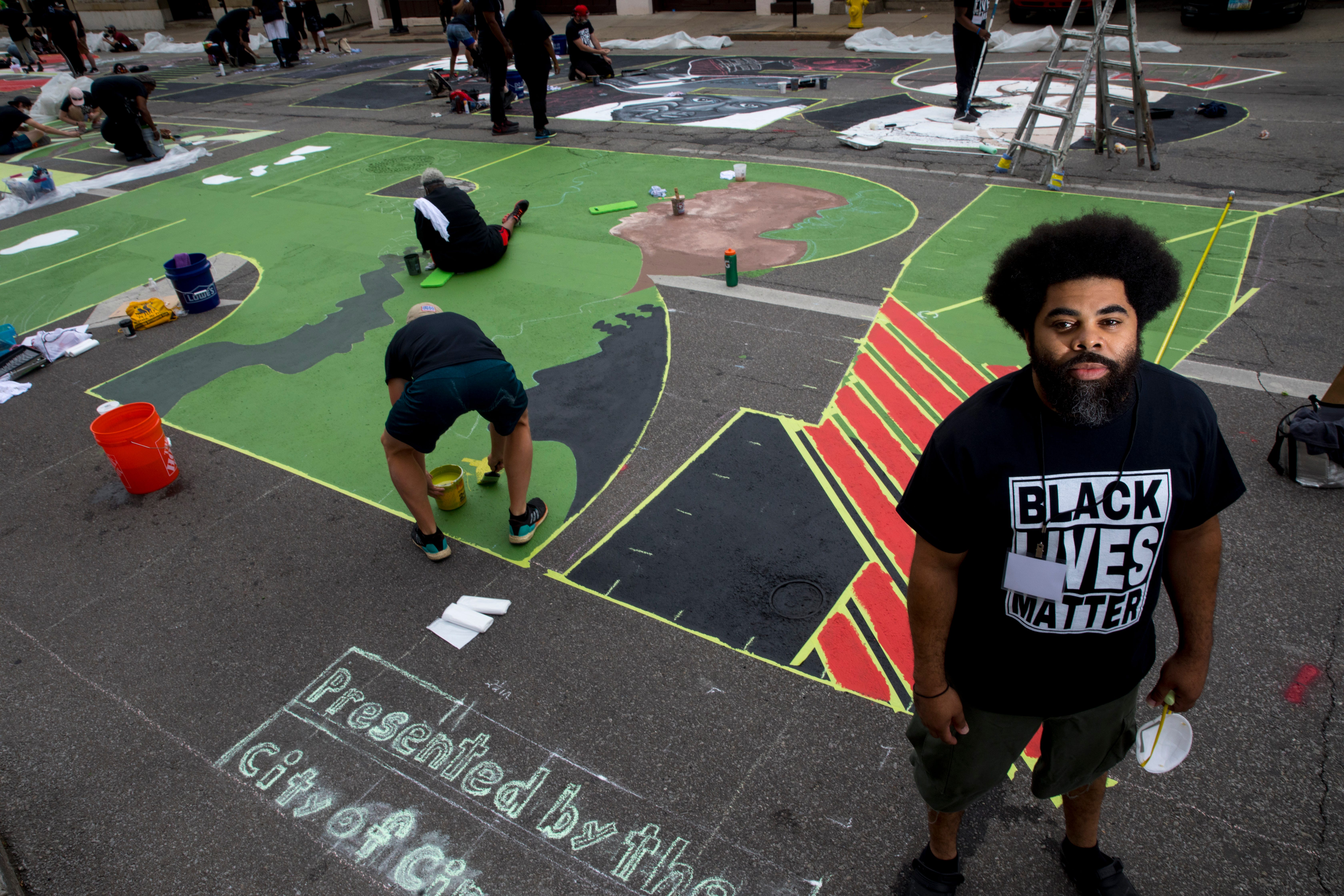 Jonathan Sears stands next to an "!" that he is creating as part of a bigger mural that reads "Black Lives Matter!" Thursday, June 18, 2020, on Plum Street in front of City Hall in Cincinnati. Seventeen local Black artists were charged with designing and creating a letter to be part of the mural. 