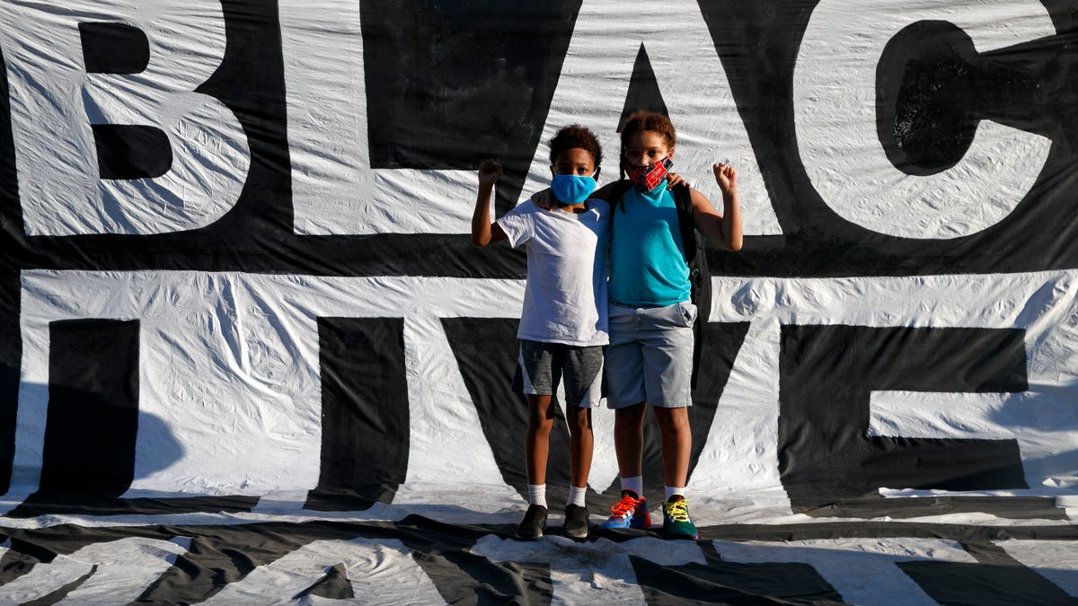 In this June 7, 2020, file photo, two young brothers stand on the Black Lives Matter banner that is draped on the fence surrounding Lafayette Park as they attend a protest near the White House in Washington.