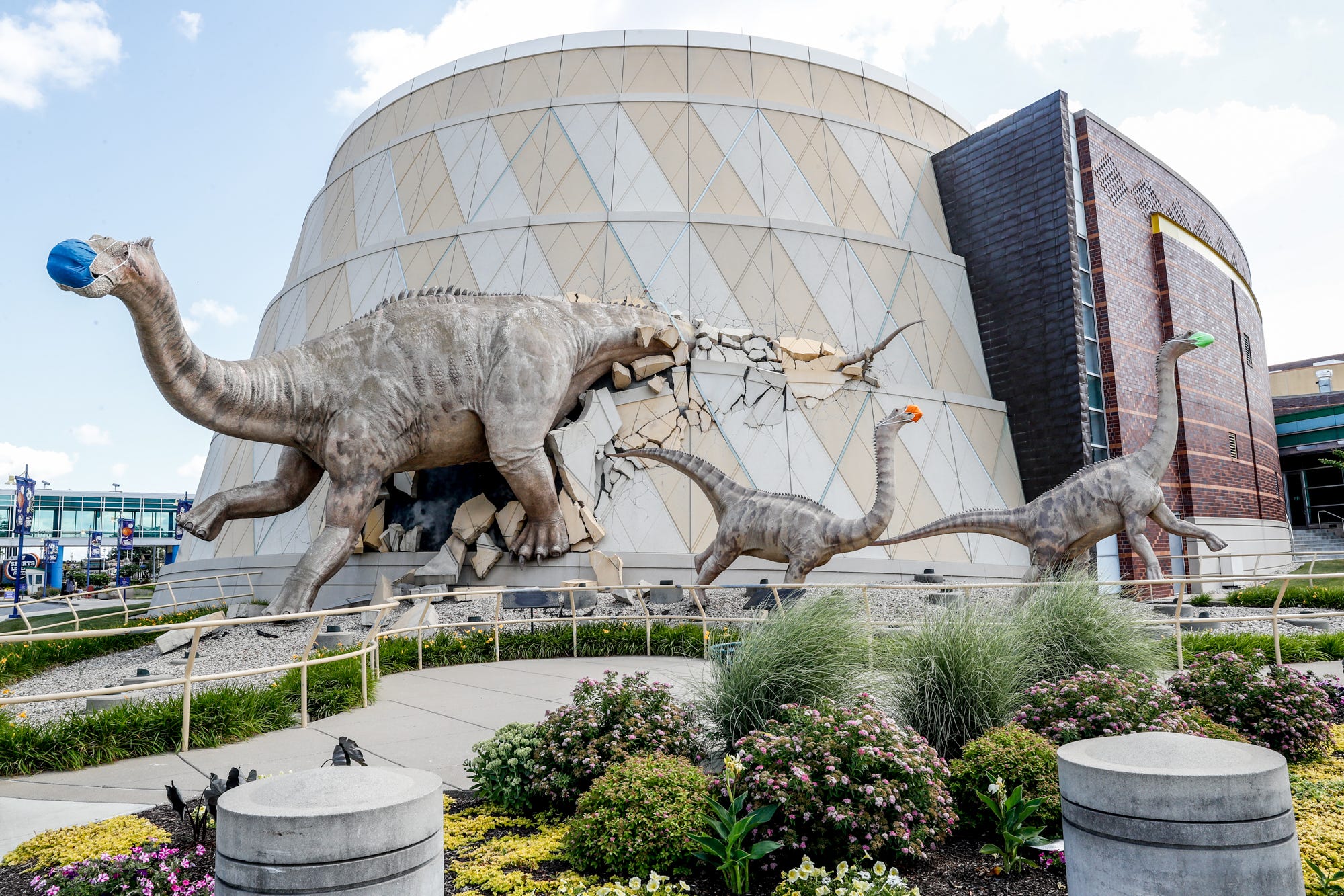 Dinosaurs outside The Children's Museum of Indianapolis wear their own masks, Wednesday, June 24, 2020. The museum was working toward reopening to the general public.