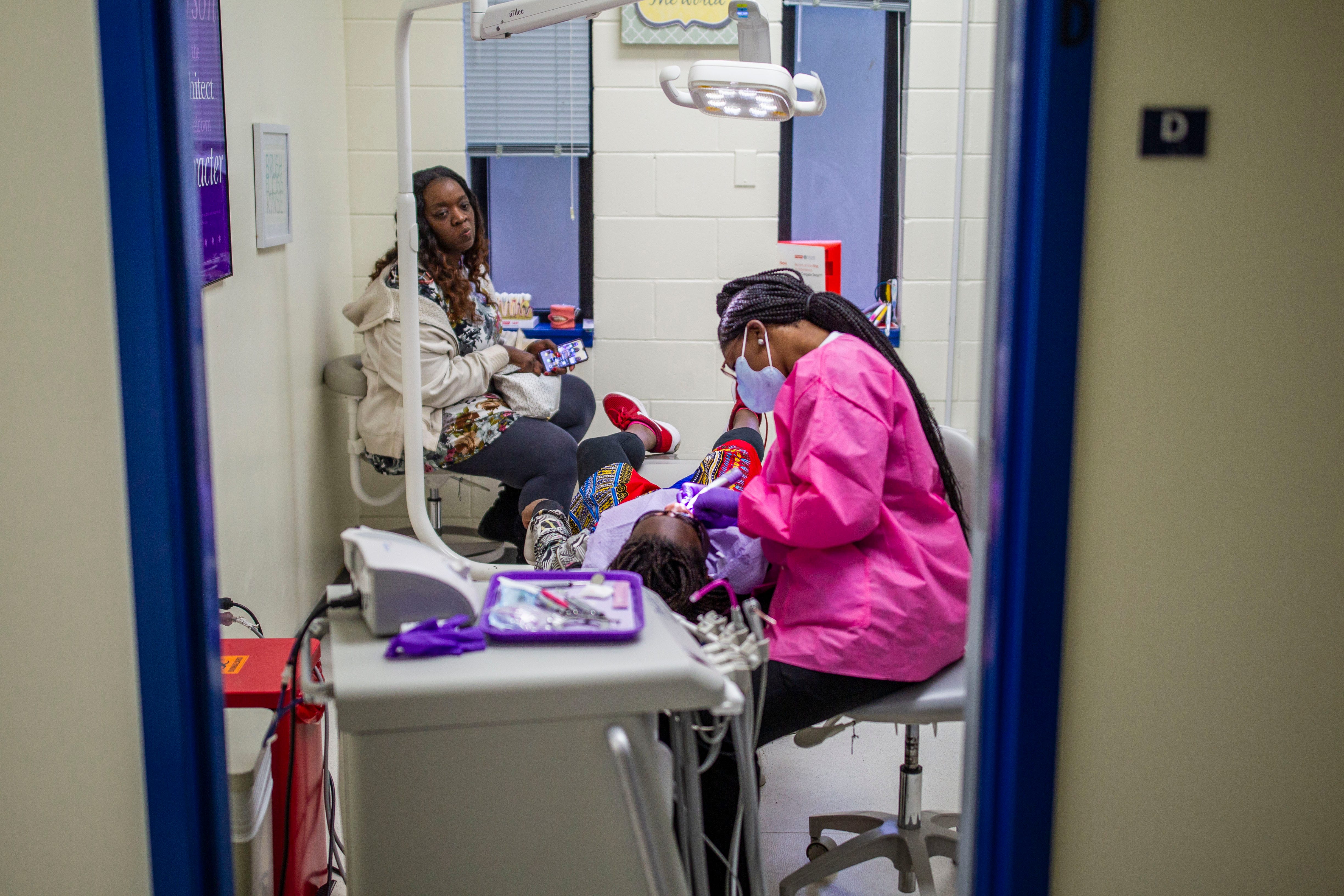 A dental hygienist cleans 11-year-old Deitra "DeeDee" Jackson’s teeth at Neighborhood Medical Center as her mom Kisha Simms, 38, looks on.