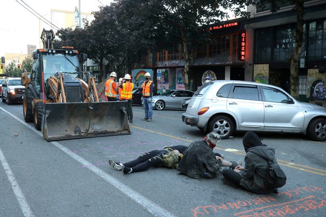 Protesters lie down and sit in the street after workers and heavy equipment from the Seattle Department of Transportation arrived at the the CHOP (Capitol Hill Occupied Protest) zone in Seattle, Friday, June 26, 2020.