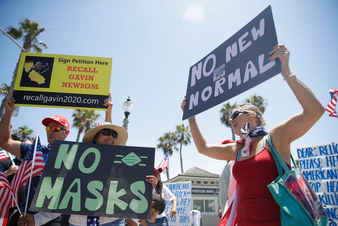 Demonstrators hold signs as they protest the lockdown and wearing masks Saturday, June 27, 2020, in Huntington Beach, Calif. (AP Photo/Marcio Jose Sanchez)