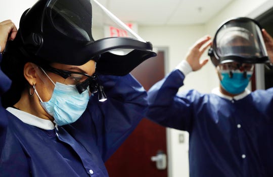 Caring Smiles Family Dentistry dentists Warren E. Woodruff, DDS, right and Amira May Woodruff, DDS, get all of their PPE on at their West Bloomfield practice before seeing patients on June 30, 2020. In addition to gowns, they are also wearing head gear that protects their faces and adds a different layer of protection.