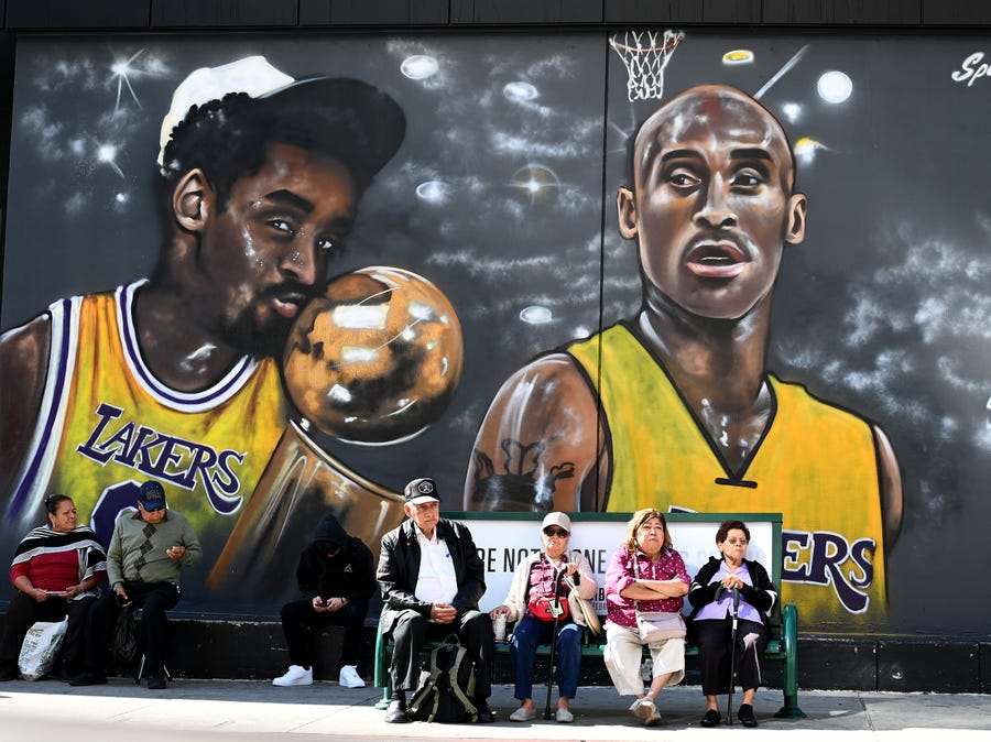 Residents wait for a bus with a mural of Kobe Bryant painted on the wall behind them in Koreatown on Feb 24, 2020, in Los Angeles.