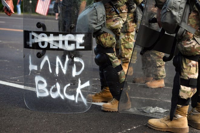 The phrase "land back" is spray painted on a National Guard riot shield and the word "police" is crossed out on Friday, July 3, in Keystone.