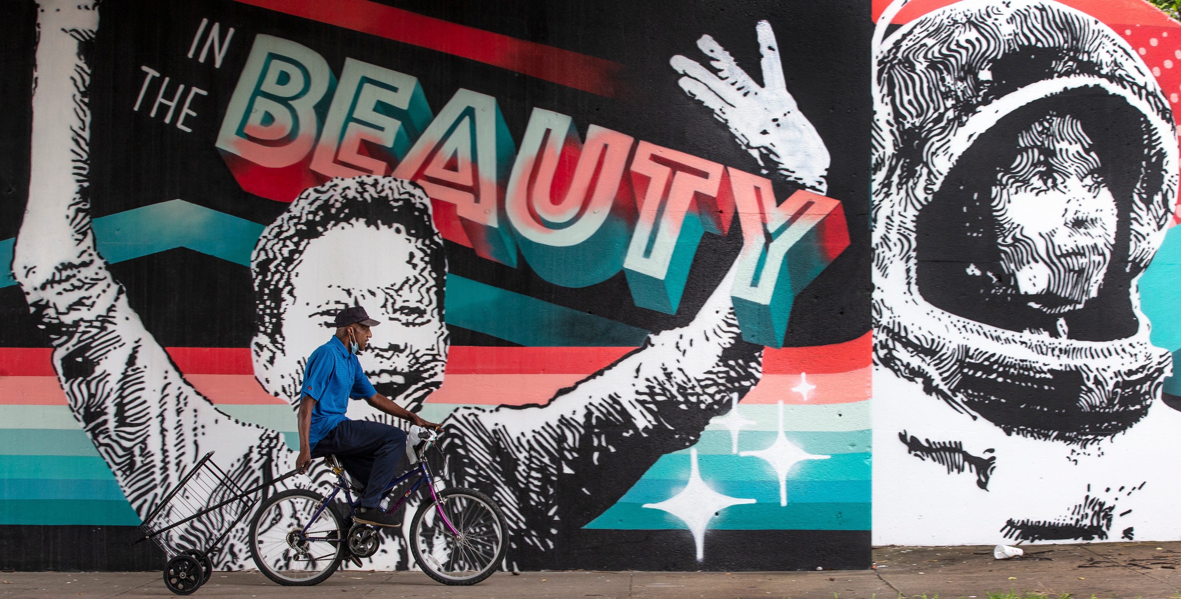 A man pulls a grocery cart behind his bike while passing an inspirational mural on Muhammad Ali Blvd in Louisville's Russell neighborhood. July 6, 2020