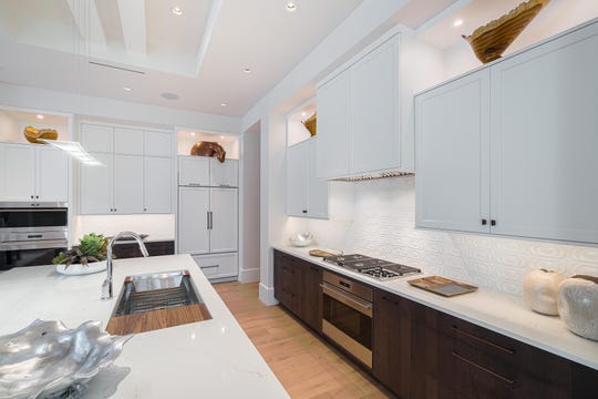 The kitchen features an elevated cabinet combination of milk chocolate-finished maple bases paired with white, beveled edge Shaker-style uppers, sable pulls and knobs, and white Pompeii quartz countertops with light veining