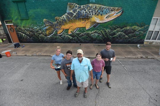 Local artist Duane Hada, front center, is creating a mural in downtown Cotter with help of Ava Obert, far left, Caleb Bailer, second from left, Michael Schraeder, far right and Breanna Hickmott. The mural is being painted on a vacation rental owned by Joey and Vanessa Peglar located at the corner of McLean Avenue and Second Street.