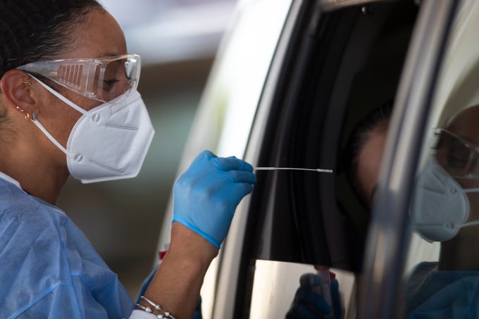 Nikila Flagg (left) tests people for COVID-19 at a drive through testing site hosted by the HeroZona Foundation in the South Mountain Community College parking lot in Phoenix, Ariz. on July 9, 2020. Tests were free and vehicles waited in a line that stretched nearly 1.5 miles from Broadway Road to Baseline Road along 24th street. Earlier in the week Arizona reached number one in the world for COVID-19 cases.