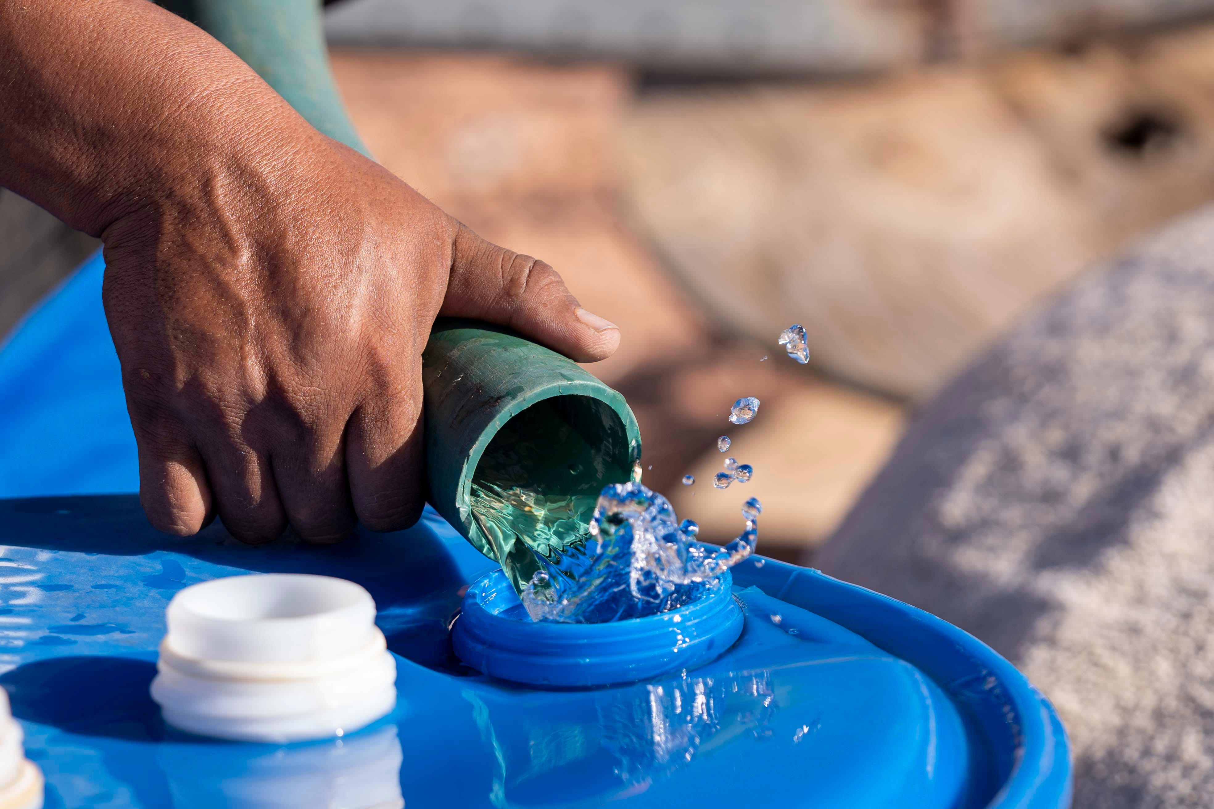 Tommy Rock uses a hose to fill a barrel at his family's home in Oljato, Utah, on the Navajo Nation.