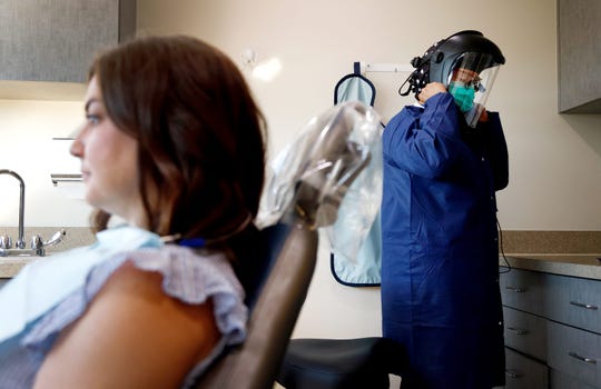 Caring Smiles Family Dentistry dental hygienist Adrienne Vasquez puts on her personal protective equipment before seeing patient Jenny Grondin on June 30, 2020, in West Bloomfield, Michigan. In addition to gowns, the dentists and other staff members are also wearing head gear that protects their faces and adds a different layer of protection. The West Bloomfield practice also has patients fill out a COVID-19 questionnaire and have their temperatures taken before they can be seen.