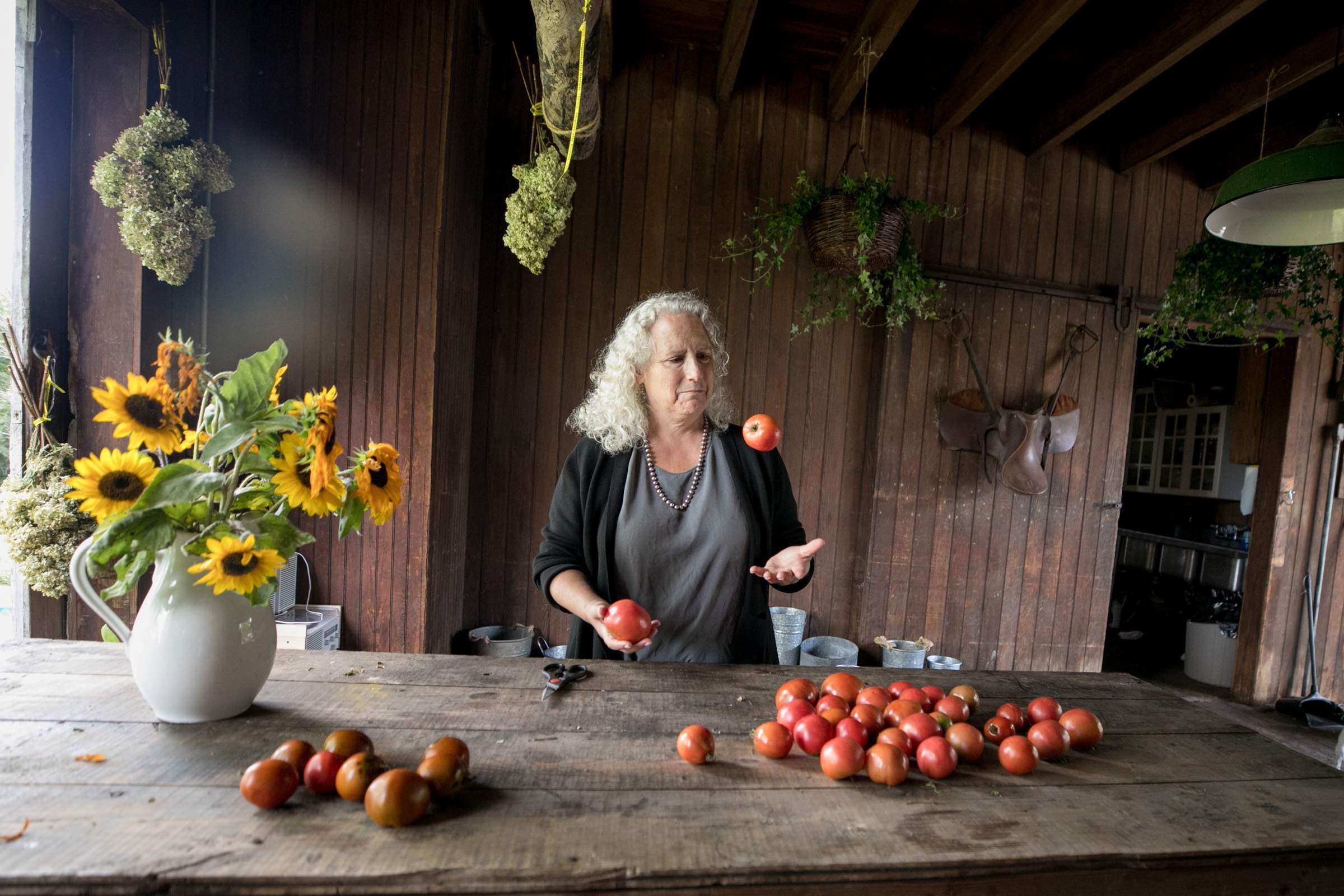 Susan Hito-Shapiro stands by a farm table covered in tomatoes and sunflowers at Goshen Green Farms.