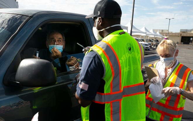 Lupe Lopez, 80, of Phoenix, takes a a testing stick to put into his nasal cavity to test himself for COVID-19 at a federal surge testing site at Maryvale High School in Phoenix, on July 17, 2020. Assisting Lopez is Phoenix firefighter Trevor Granger, center, and Susan Schubert, a nurse, The surge testing site which is free will continue at Maryvale High School for 12 days. Lopez tested positive for COVID-19 on June 29 and was hospitalized. He was released from the hospital on July 6.