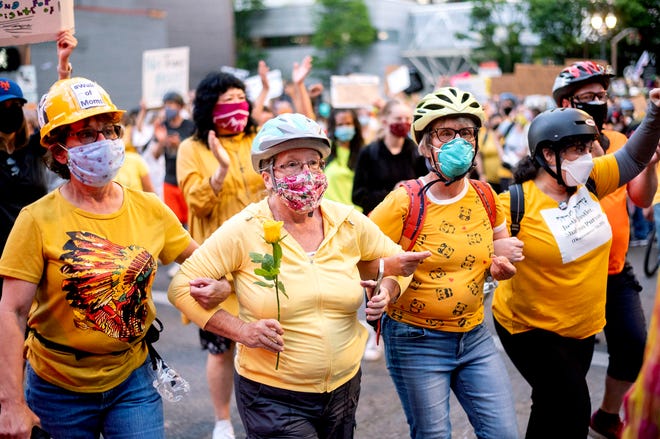 Norma Lewis holds a flower while forming a "wall of moms" during a Black Lives Matter protest on Monday, July 20, 2020, in Portland, Oregon.