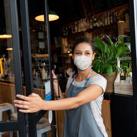 A business owner opens the door at a cafe wearing 
