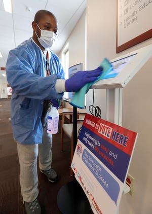 Kevin Collins cleans the surface of a voter registration kiosk at Progressive Community Health Center. Patients who go in for check-ups can register to vote at the same time.