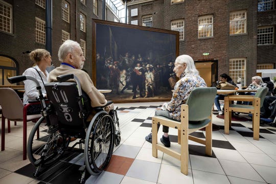 Residents of the Dr. Sarphati House nursing home in Amsterdam, The Netherlands, sit in front of a same size version of the famous painting 'The Night Watch' by Dutch painter Rembrandt van Rijn, in Amsterdam on July 20, 2020. - This summer, the Rijksmuseum brings a version of the world-famous painting by Rembrandt to thirty nursing and care homes and senior complexes. Outings to cultural institutions are not possible for many elderly people due to the coronavirus crisis.