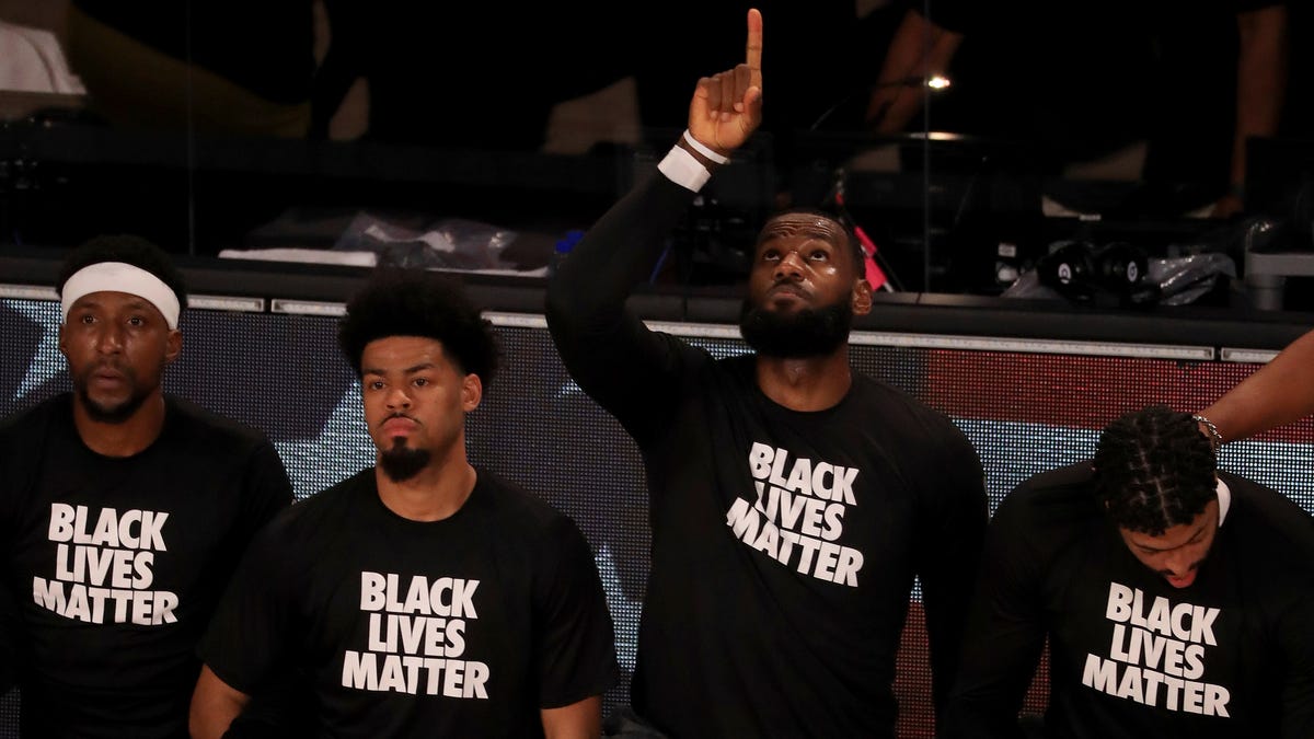 Los Angeles Lakers' LeBron James wears a Black Lives Matter shirt as he points up and kneels with teammates during the national anthem prior to their opening game in the NBA bubble.