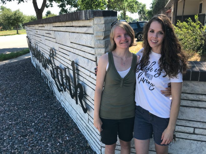 Lily Horst, left, and Rachel Dozier pose in front a restored sign at the intersection of Drake Road and Meadowlark Avenue on Friday, July 31, 2020. The sign was restored in honor of Dozier's late husband, Andre Dozier.
