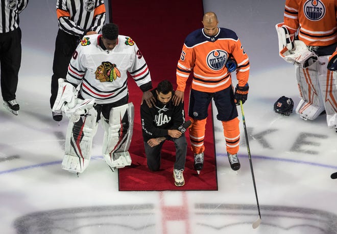 Minnesota Wild's Matt Dumba takes a knee during the national anthem while flanked by Edmonton Oilers' Darnell Nurse, right, and Chicago Blackhawks' Malcolm Subban.