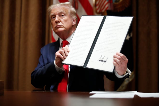 President Donald Trump holds up a signed Executive Order on hiring American workers, during a meeting with U.S. tech workers, in the Cabinet Room of the White House, Monday, Aug. 3, 2020, in Washington.
