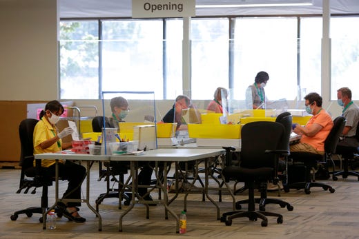 Election workers are spaced out and separated by screens for protection from the coronavirus as they open envelopes containing ballots for the Aug. 4 Washington state primary at King County Elections in Renton, Wash. on Aug. 3, 2020.