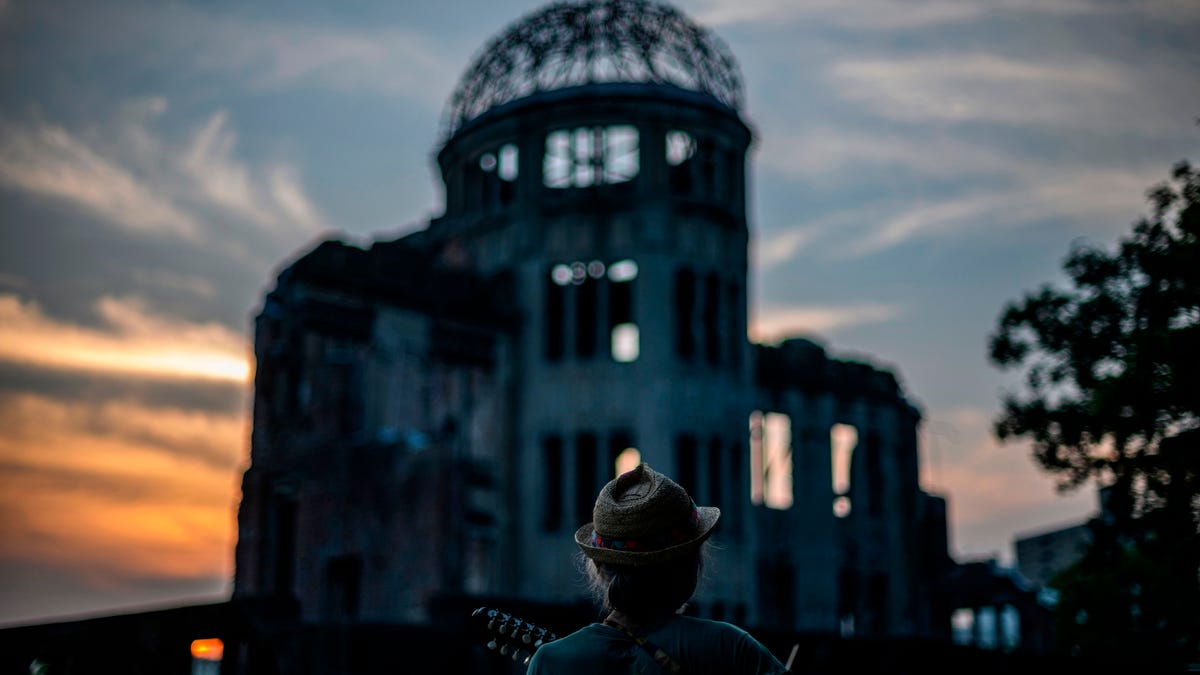 A man plays his guitar in front of  in front of ruins of the Hiroshima Prefectural Industrial Promotion Hall, now commonly known as the atomic bomb dome, during sunset in Hiroshima on August 5, 2020.  Japan on August 6, 2020 marks 75 years since the world's first atomic bomb attack, with the COVID-19 coronavirus pandemic forcing a scaling back of annual ceremonies to commemorate the victims.