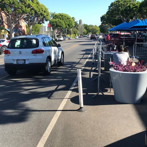 An SUV passes by the outdoor dining areas for a pi
