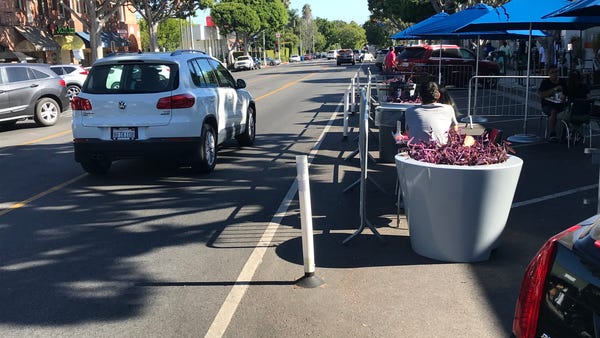 An SUV passes by the outdoor dining areas for a pi