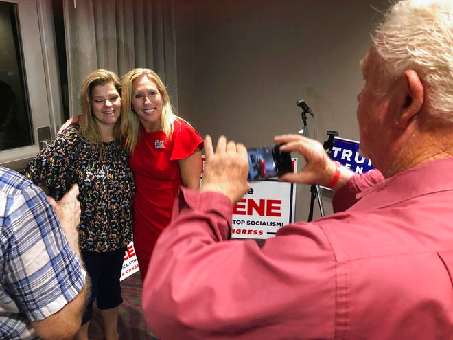 Supporters take photos with construction executive Marjorie Taylor Greene, background right, late Tuesday, Aug. 11, 2020, in Rome, Ga. Greene, criticized for promoting racist videos and adamantly supporting the far-right QAnon conspiracy theory, won the GOP nomination for northwest Georgia's 14th Congressional District. (AP Photo/Mike Stewart)