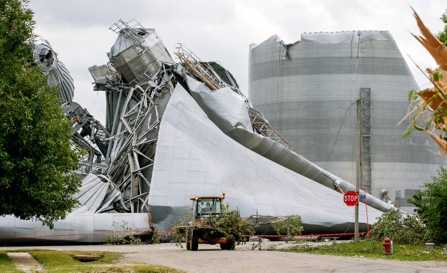 Iowa Department of Transportation workers help with tree debris removal as grain bins from the Archer Daniels Midland facility are seen severely damaged in Keystone, Iowa, on Wednesday, Aug. 12, 2020. A storm slammed the Midwest with straight-line winds of up to 100 mph on Monday.