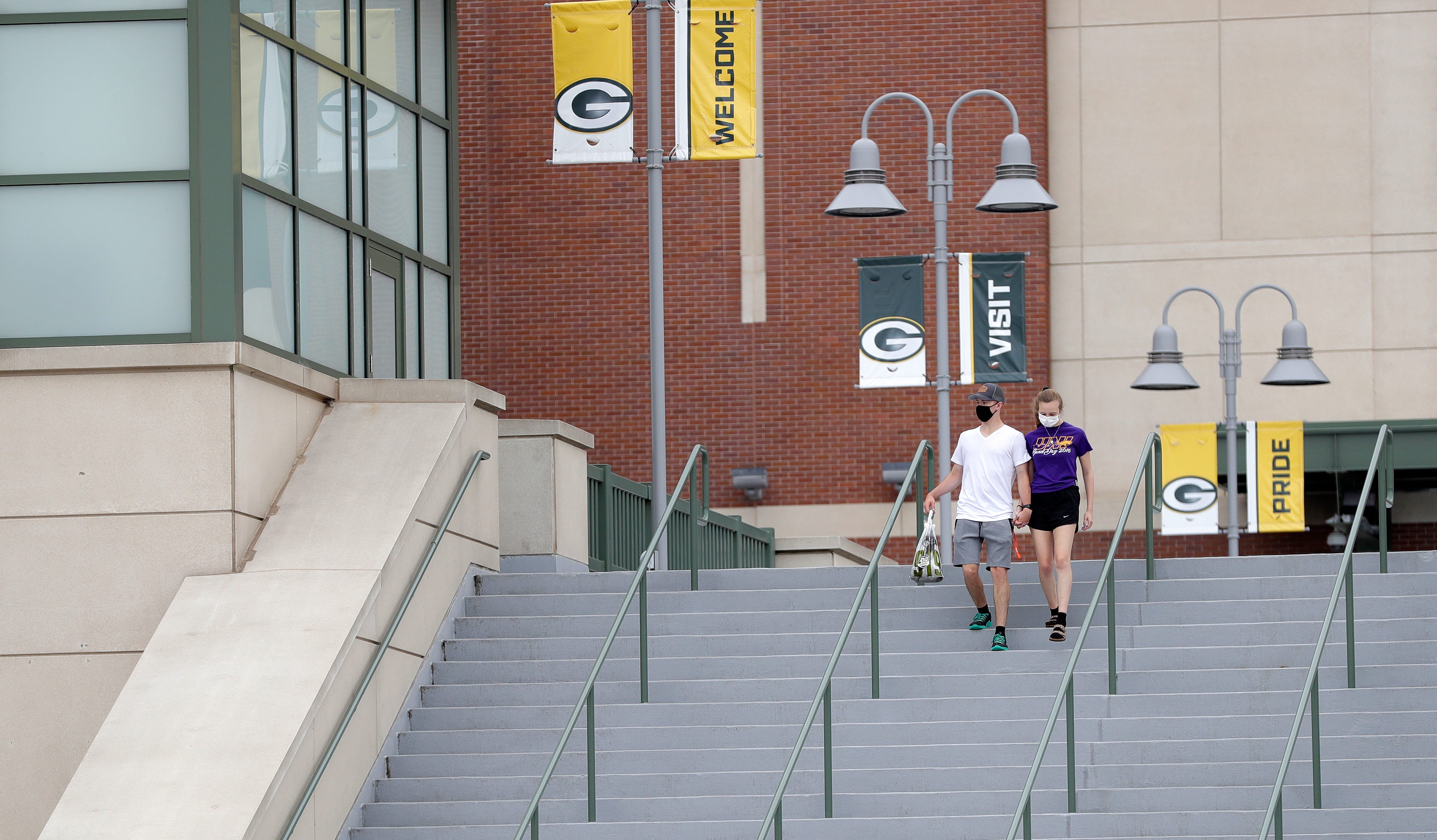 A couple wearing masks walks down the steps at Lambeau Field on Aug. 15, 2020, in Green Bay, Wis. The Green Bay Packers held their first practice of training camp at Ray Nitschke Field, but with no public viewing due to the coronavirus pandemic, only a few fans visited the area.