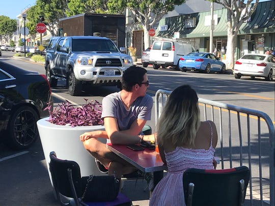 A pair of diners sit at a restaurant table in the street on Larchmont Boulevard section of Los Angeles, separated from traffic by only a metal fence and protected by only a planter