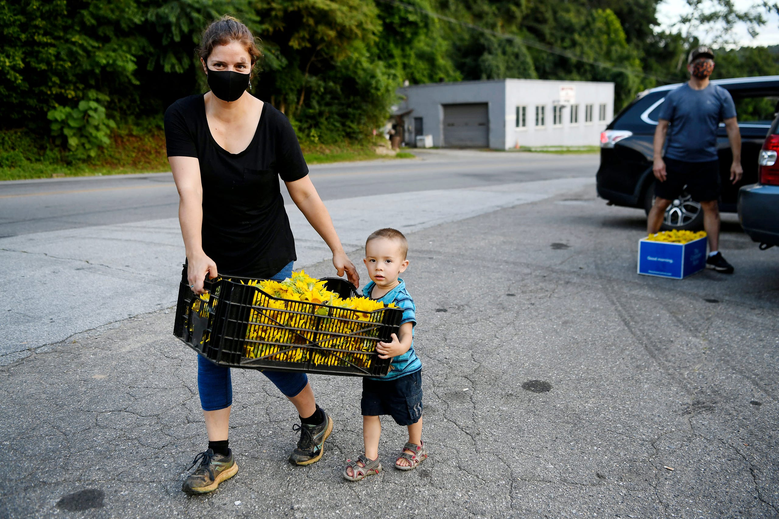 Arica Haro carries a load of sunflowers with help from her two-year-old son, Forest, as residents of the Olivette community spread cheer across the Craggy Bridge in Woodfin August 19, 2020. "It's been quite the year," said Banzer, "so this is exciting, to spread a little happiness and to have the opportunity to get a smile."