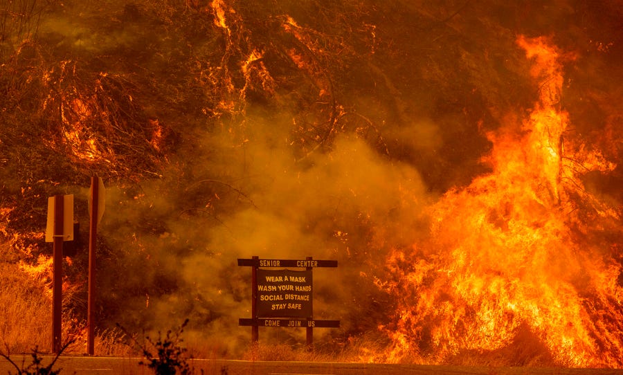 A sign warning people about COVID-19 is surrounded by flames from the Hennessey fire near Napa, Calif., on Aug. 18.