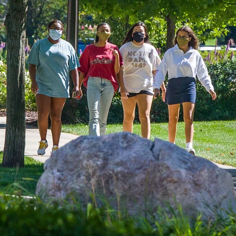 Students wearing masks walk on campus of the Unive