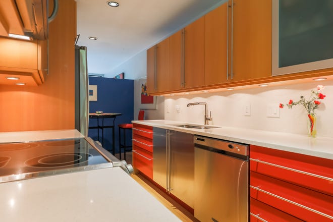 The long, galley kitchen keeps its original design, but with new surfaces of beech wood, red-orange lacquered drawers and white quartz counters. The blue wall at the rear shows the low profile, which lets in sunlight.