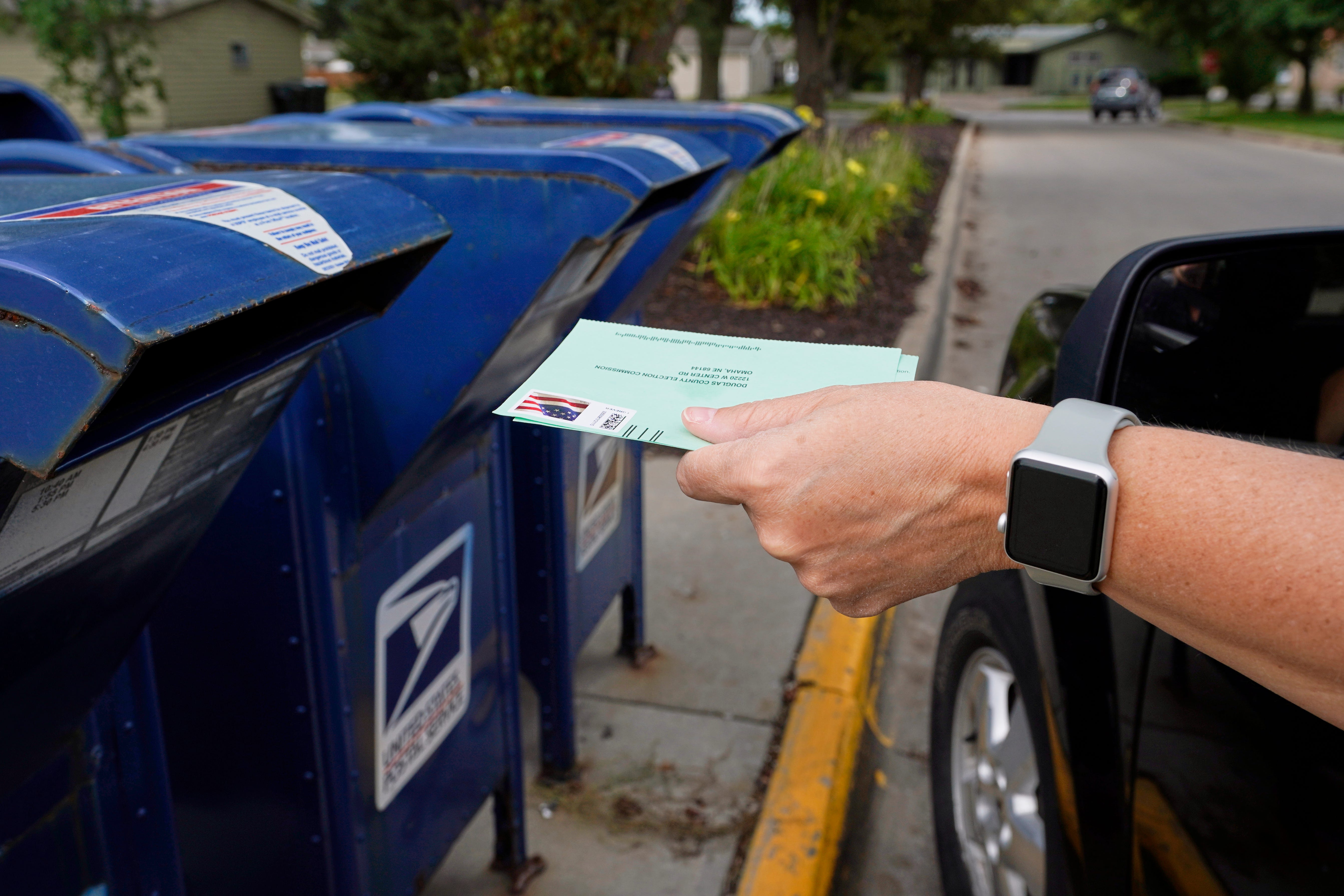 A person drops applications for mail-in-ballots into a mail box in Omaha, Neb. U.S. Postal Service warnings that it can’t guarantee ballots sent by mail will arrive on time have put a spotlight on the narrow timeframes most states allow to request and return those ballots.