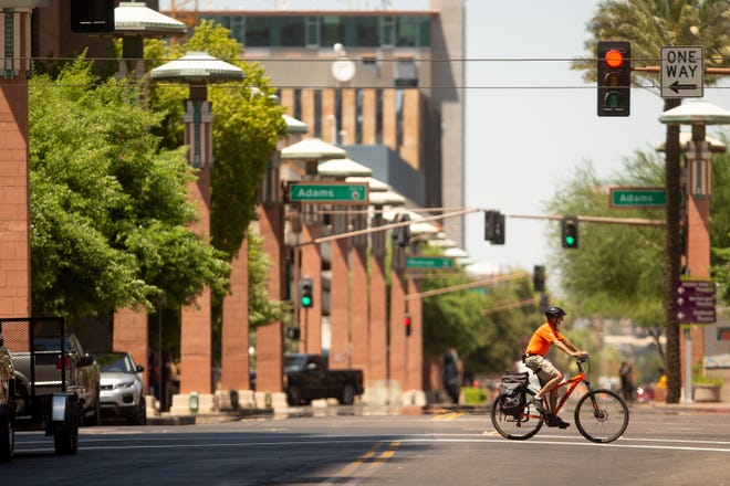 A downtown Phoenix ambassador wearing a mask during the COVID-19 pandemic rides his bicycle across the intersection of Adams Street and 2nd Street on July 15, 2020.
