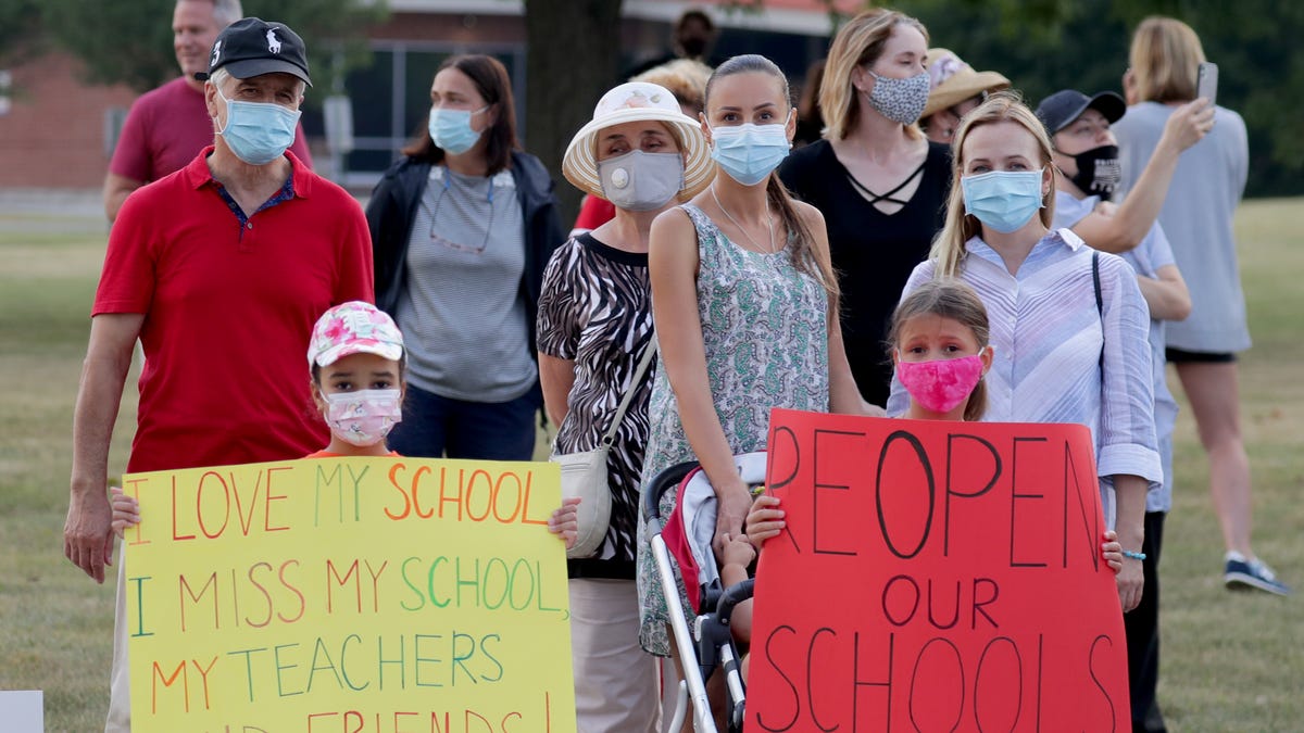 Diana Mejia, left, and Anna Sofiya Iskra, both 8, hold signs while with their mothers, Olga Mejia, second right, and Olena Iskra, far right, during a protest Sunday, Aug. 23, 2020, at Homestead High School of the decision by the Mequon-Thiensville School District to keep schools closed in the fall.